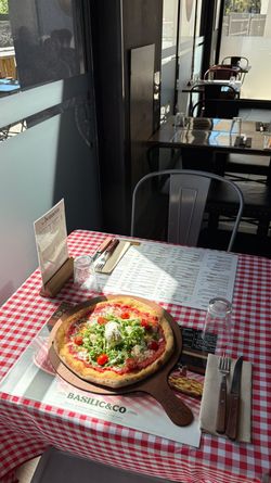 Pizza artisanale servie sur planche en bois dans un restaurant avec table à carreaux rouges et blancs.