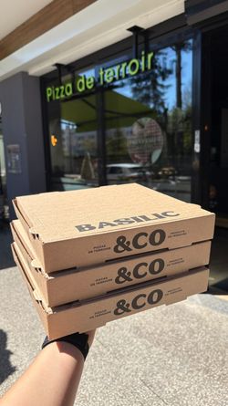 Boîtes à pizza empilées à emporter devant le restaurant Basilic & Co à Voiron, spécialisé en pizza artisanale.