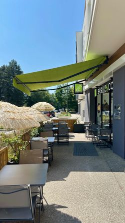 Terrasse extérieure de Basilic & Co à Voiron avec tables, chaises et store vert sous un ciel bleu clair.