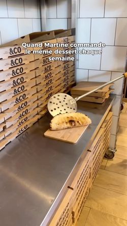 Boîte à pizza empilées sur un comptoir en inox avec une pizza artisanale découpée devant.