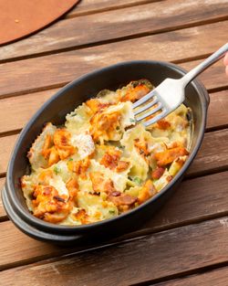 Plat de ravioles gratinées servies dans un plat noir sur une table en bois, avec une fourchette en action.