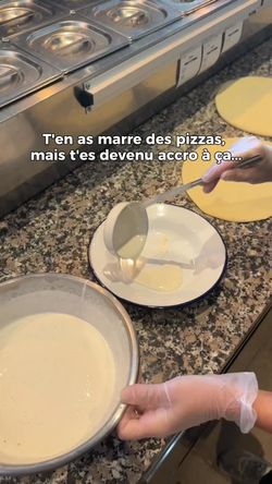 Préparation d'une pizza artisanale avec de la pâte et une sauce blanche versée dans une assiette dans une cuisine