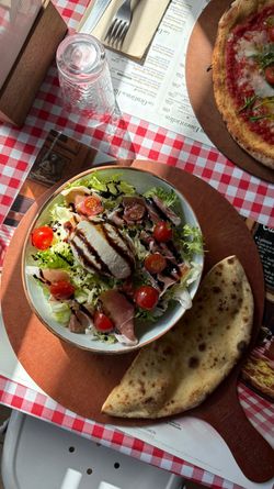 Salade avec tomates cerises, jambon, fromage, vinaigrette balsamique et galette sur table à carreaux rouges.