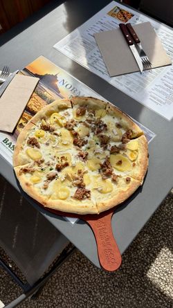 Pizza artisanale avec fromage fondu et viande, servie sur une planche en bois sur une table avec menus et couverts.