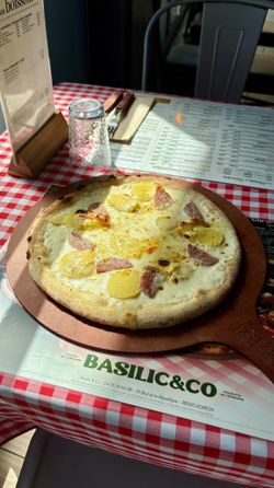 Pizza artisanale avec pommes de terre et lardons sur une planche en bois au restaurant Basilic & Co à Voiron.