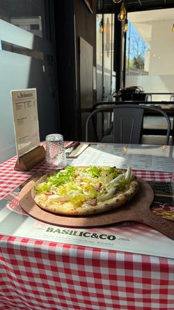 Pizza artisanale garnie de salade fraîche servie sur une planche en bois à Basilic & Co à Voiron