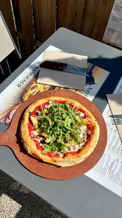 Pizza artisanale garnie de roquette, champignons et sauce tomate sur une table avec couverts et menus Basilic & Co à Voiron