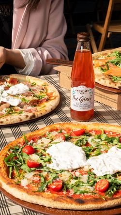 Pizza artisanale garnie de roquette, tomates cerises et burrata, accompagnée d'une bouteille de thé glacé hibiscus.