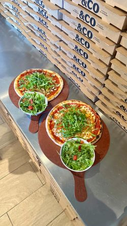 Deux pizzas artisanales garnies de roquette et deux salades fraîches servies sur planches en bois à Basilic & Co Voiron