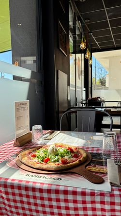 Pizza artisanale garnie de salade fraîche et tomates, servie sur une table à nappes rouges et blanches chez Basilic & Co
