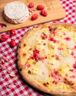 Pizza artisanale avec pâte fine et garniture fromagère, accompagnée d'un fromage sur une planche en bois.