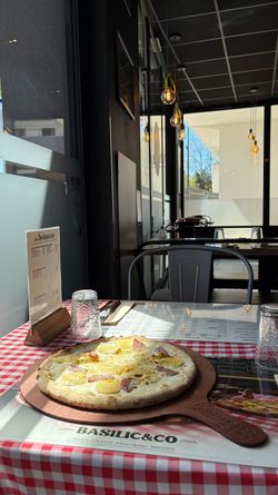 Pizza artisanale à croûte fine servie sur une table à nappe à carreaux rouges dans le restaurant Basilic & Co