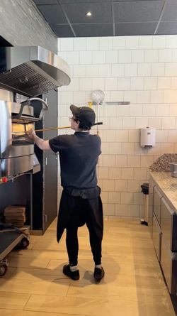 Employé en train de cuire une pizza dans un four à pizza dans un restaurant Basilic & Co - pizzas de terroirs - Voiron