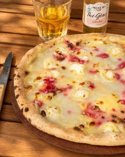 Pizza artisanale servie sur une assiette en bois, accompagnée d'un verre et d'une bouteille de thé glacé pêche.
