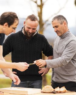 Trois hommes discutant autour d'une table en extérieur avec pain et pizza artisanale visible.