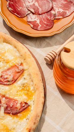 Pizza artisanale avec tranches de charcuterie sur une assiette et pot de miel à côté