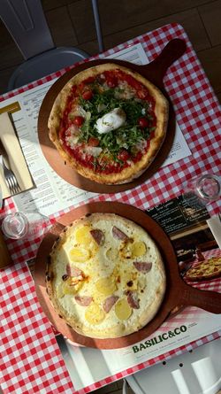 Deux pizzas artisanales sur planche en bois, posées sur une table à carreaux rouges et blancs dans un restaurant.