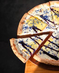 Pizza artisanale garnie de fromage, sauce blanche et pétales de fleurs comestibles sur fond sombre.