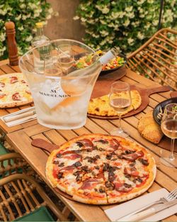 Pizza artisanale et salades posées sur une table en bois avec des verres de vin rosé et un seau à glace