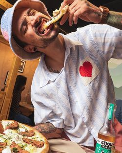 Jeune homme mangeant une pizza artisanale chez Basilic & Co avec une boisson en bouteille à côté.