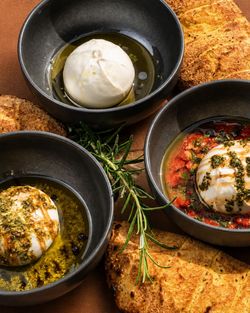 Burrata servie dans des bols noirs avec différentes sauces et accompagnée de pain grillé et romarin.