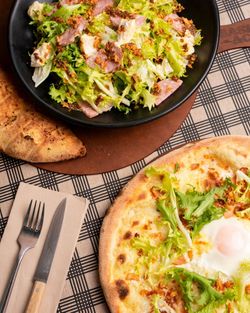 Salade verte et pizza artisanale avec œuf au plat, servies avec couverts sur table à carreaux chez Basilic & Co.