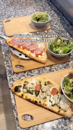 Deux demi-pizzas artisanales servies avec des salades sur planches en bois, prêtes à emporter ou en livraison.
