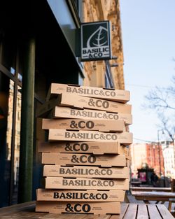 Pile de boîtes à pizza Basilic & Co empilées devant le restaurant avec enseigne visible en extérieur.