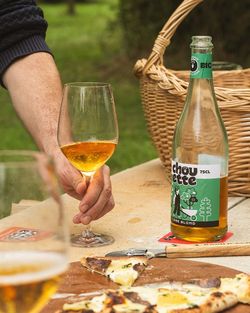 Pizza artisanale avec une bouteille de cidre blond et un verre, sur une table en bois près d'un panier en osier.