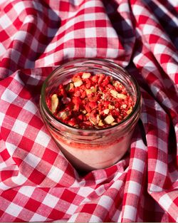Dessert en verrine avec morceaux de fruits rouges et noix sur nappe à carreaux rouges et blancs.