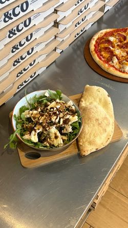 Salade fraîche avec fromage et vinaigrette balsamique, calzone doré et pizza artisanale à côté des boîtes à pizza empilées.