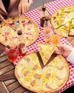 Trois pizzas artisanales variées sur une table en bois avec des boissons et des bouteilles d'arômes.
