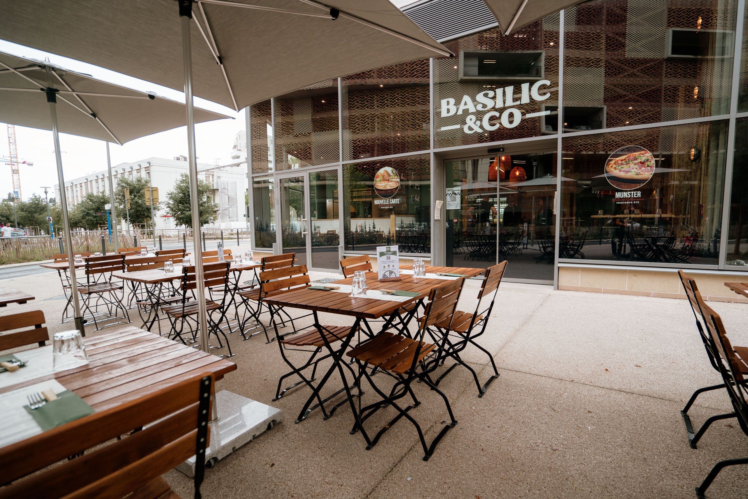 Terrasse extérieure du restaurant Basilic & Co avec des tables et chaises en bois, offrant un cadre convivial.