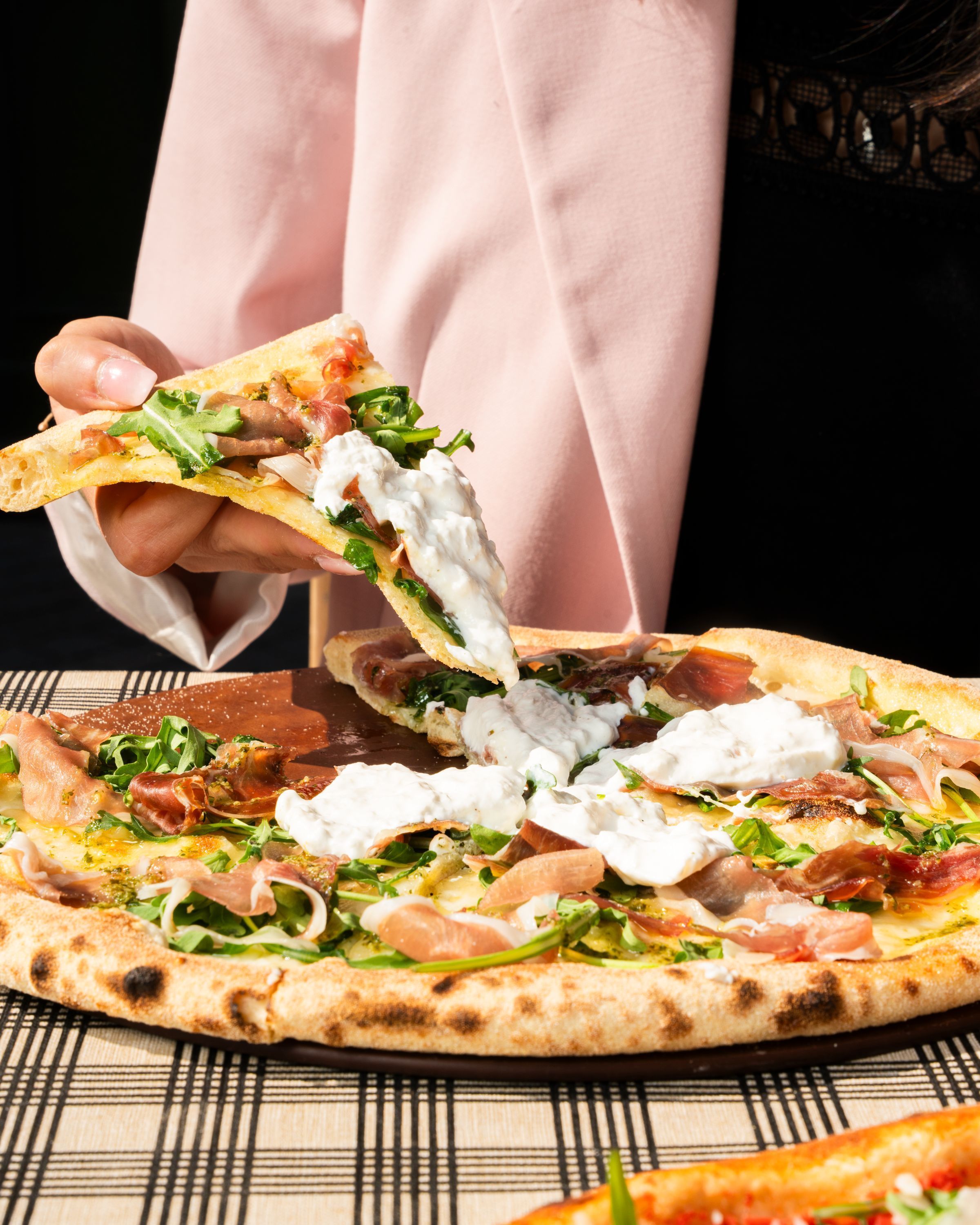 Dégustation d'une pizza artisanale garnie de roquette et de crème. Pizzas à emporter disponibles.