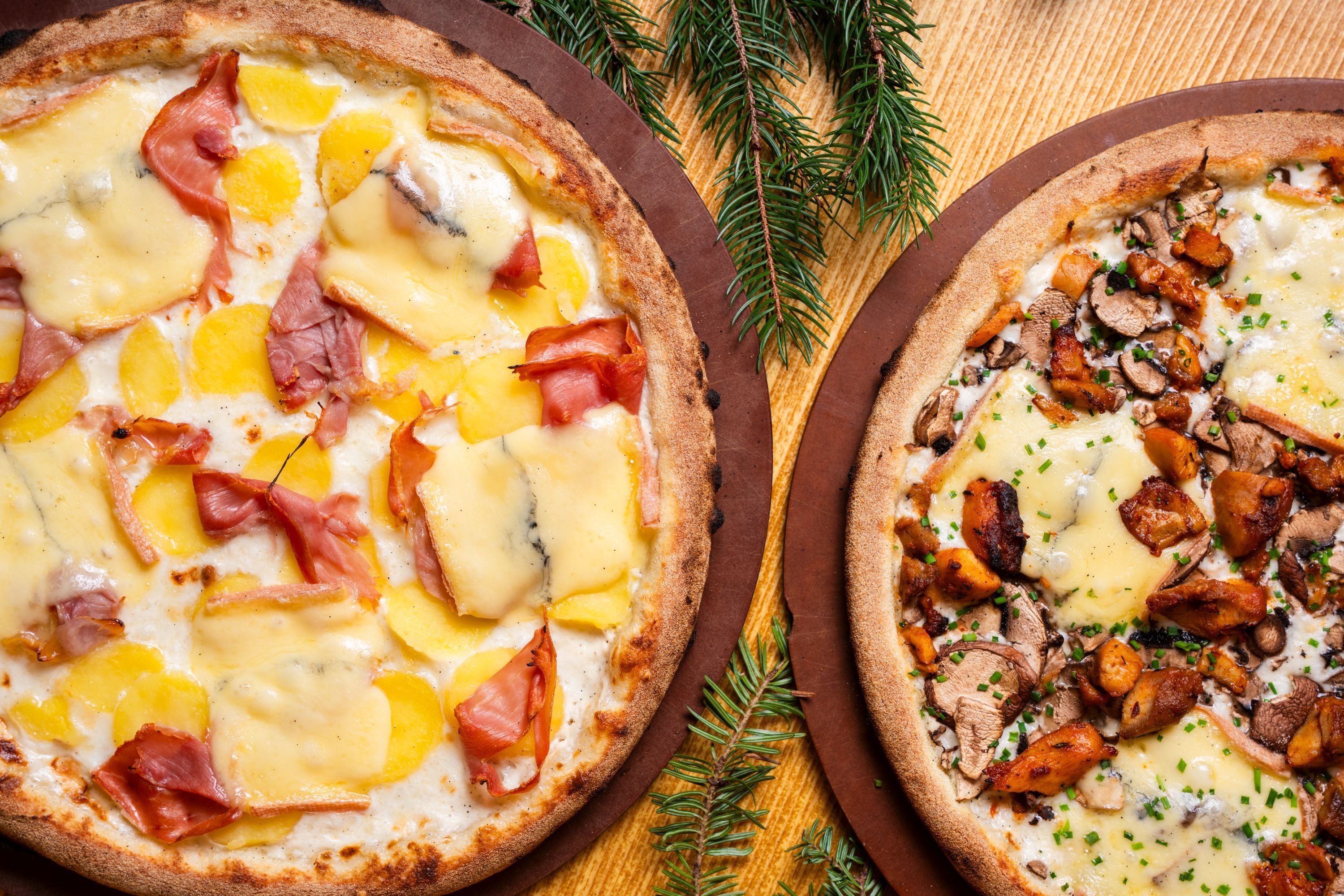 Pizzas artisanales garnies de fromage, jambon et fruits, sur des plaques en bois.