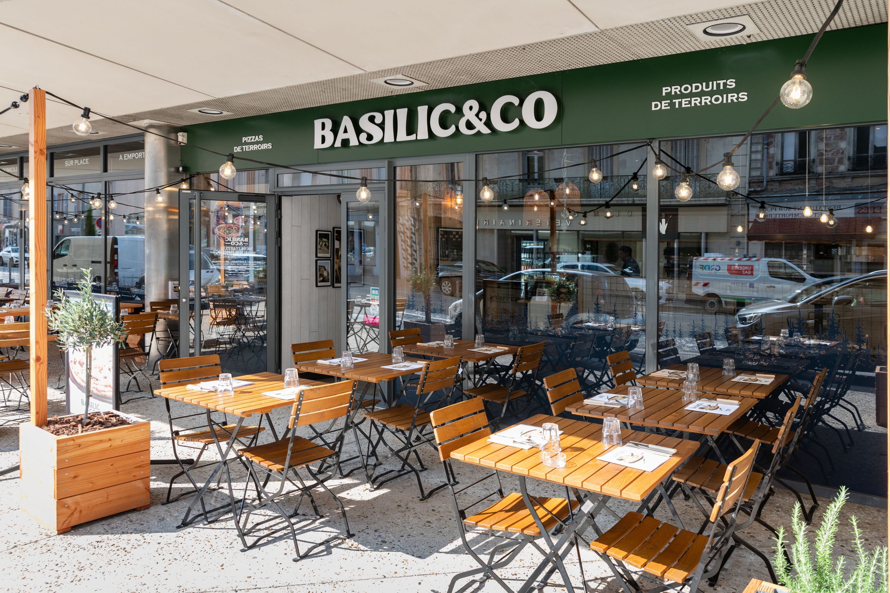 Terrasse du restaurant Basilic & Co avec des tables en bois et chaises, ambiance accueillante pour déguster des pizzas.