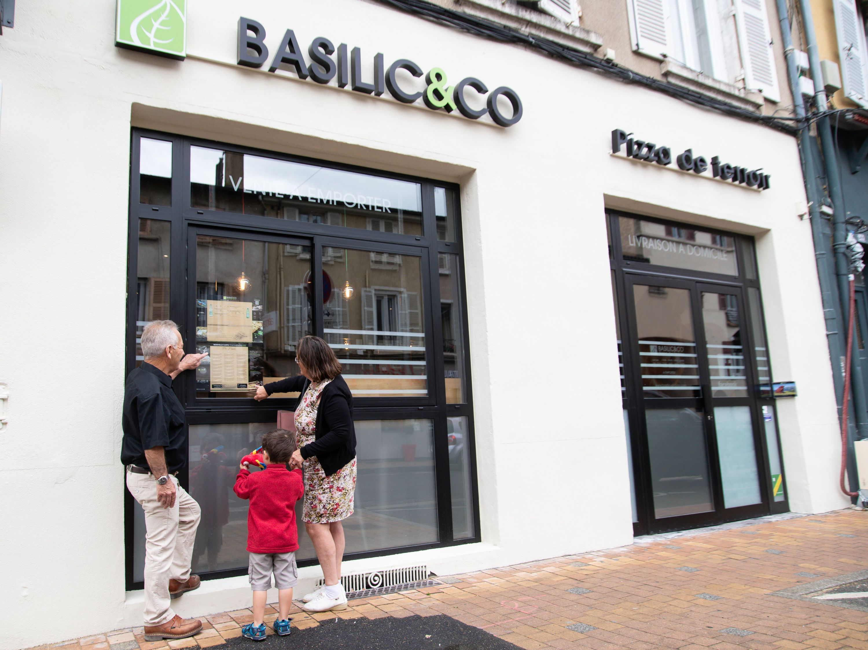 Un couple et un enfant regardent le menu à emporter de Basilic & Co à Villefranche-sur-Saône.