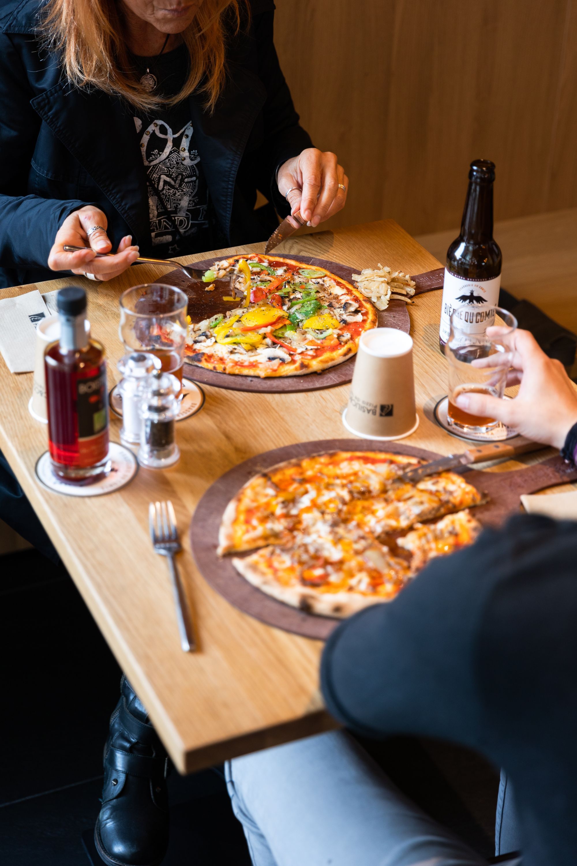 Deux pizzas artisanales servies sur une table avec boissons et condiments.