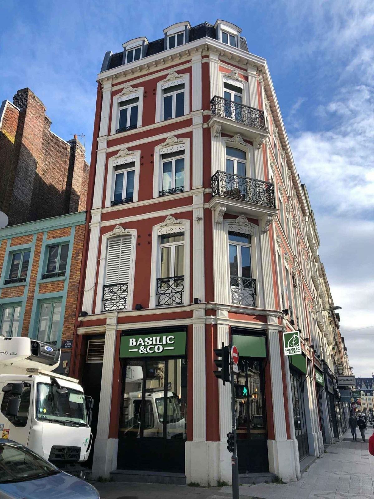 Façade d'un bâtiment ancien avec la devanture verte de Basilic & Co, spécialisé en pizza artisanale à emporter