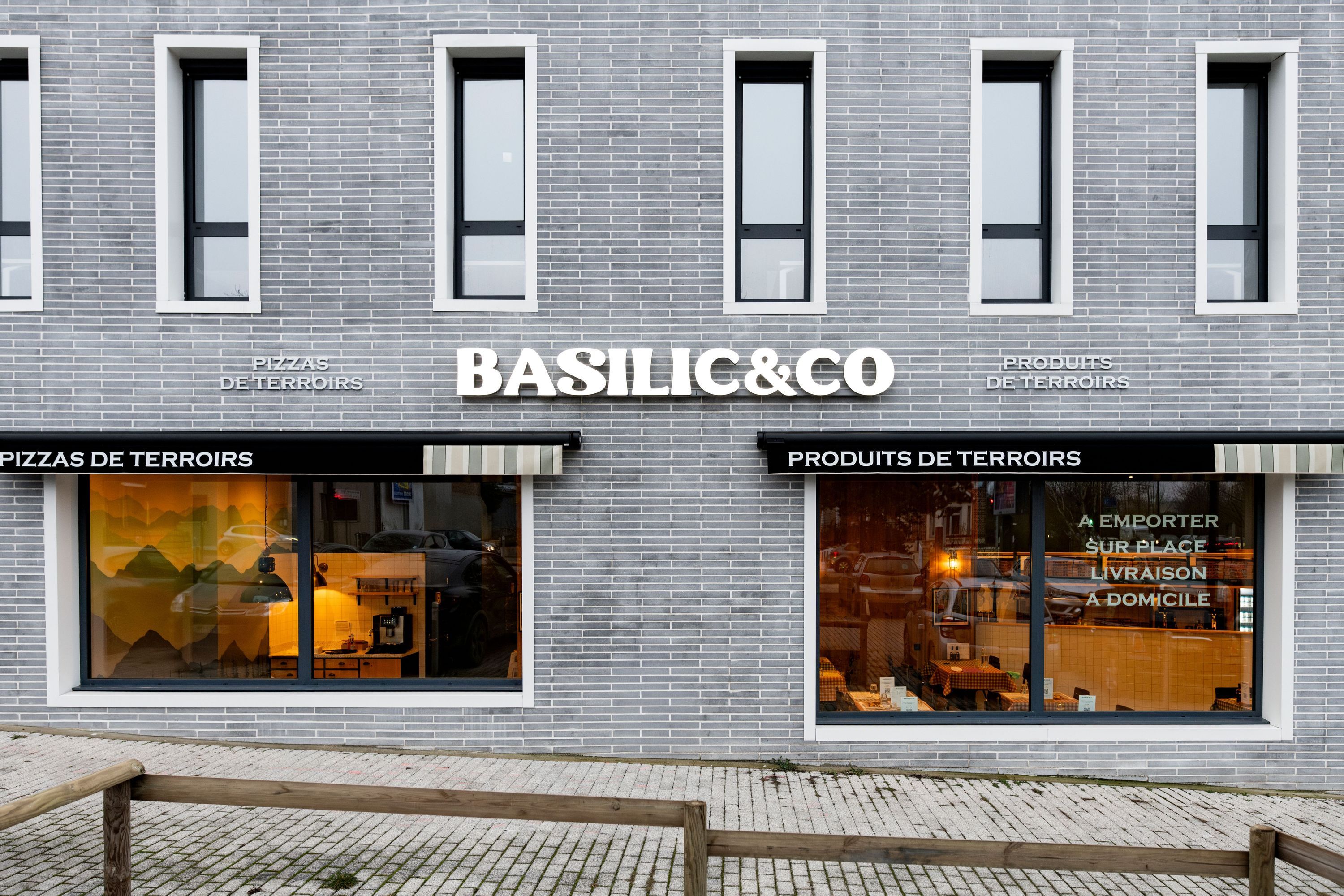 Façade en briques grises du restaurant Basilic & Co à Amiens avec fenêtres et enseigne lumineuse blanche.