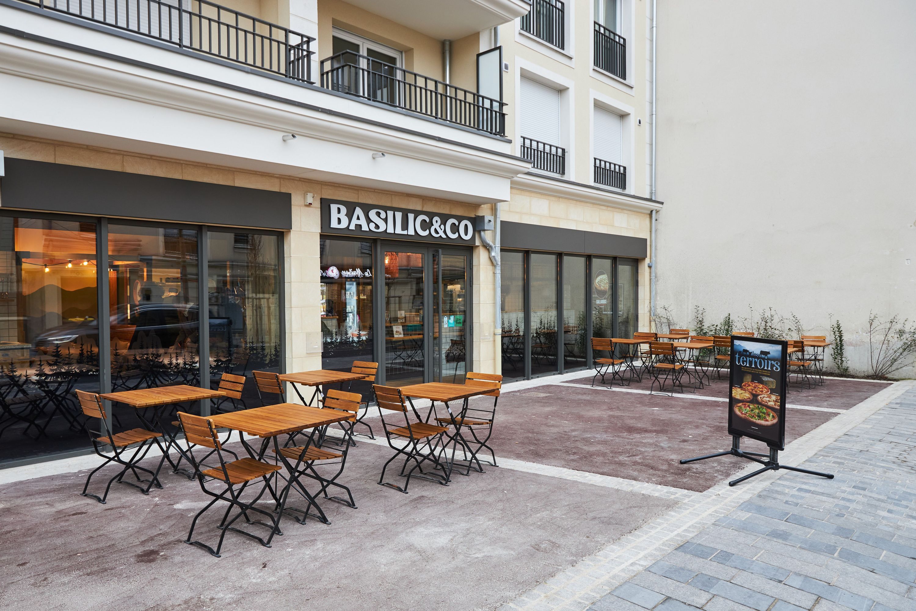 Terrasse du restaurant Basilic & Co à Sartrouville, avec tables en bois et chaises pour déguster des pizzas.