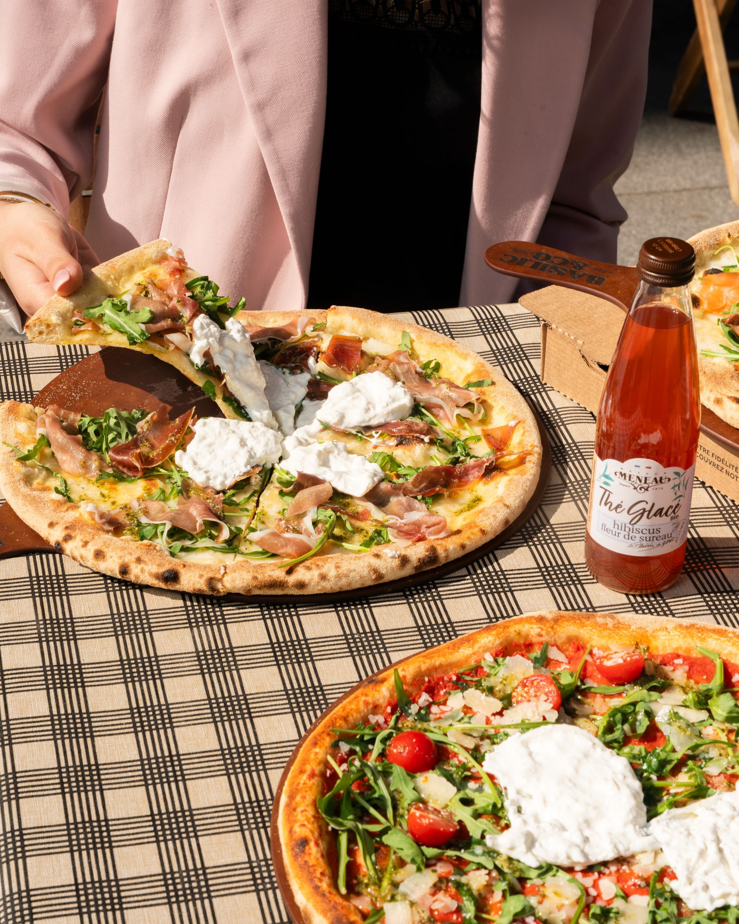 Pizza artisanale avec mozzarella et jambon servie à emporter, accompagnée de salade et boisson glacée.