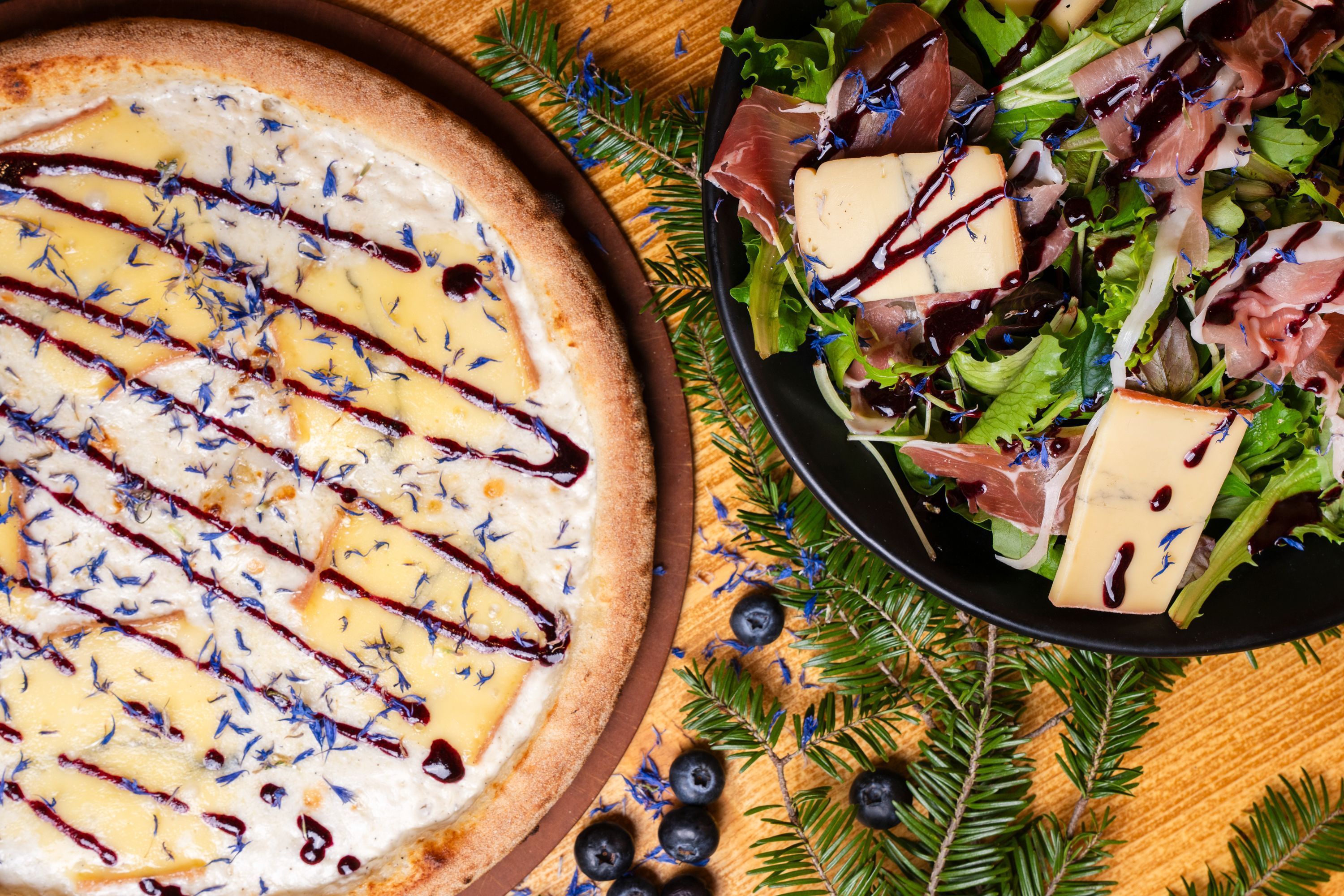 Pizzas artisanales accompagnées de salades fraîches, sur une table en bois décorée.