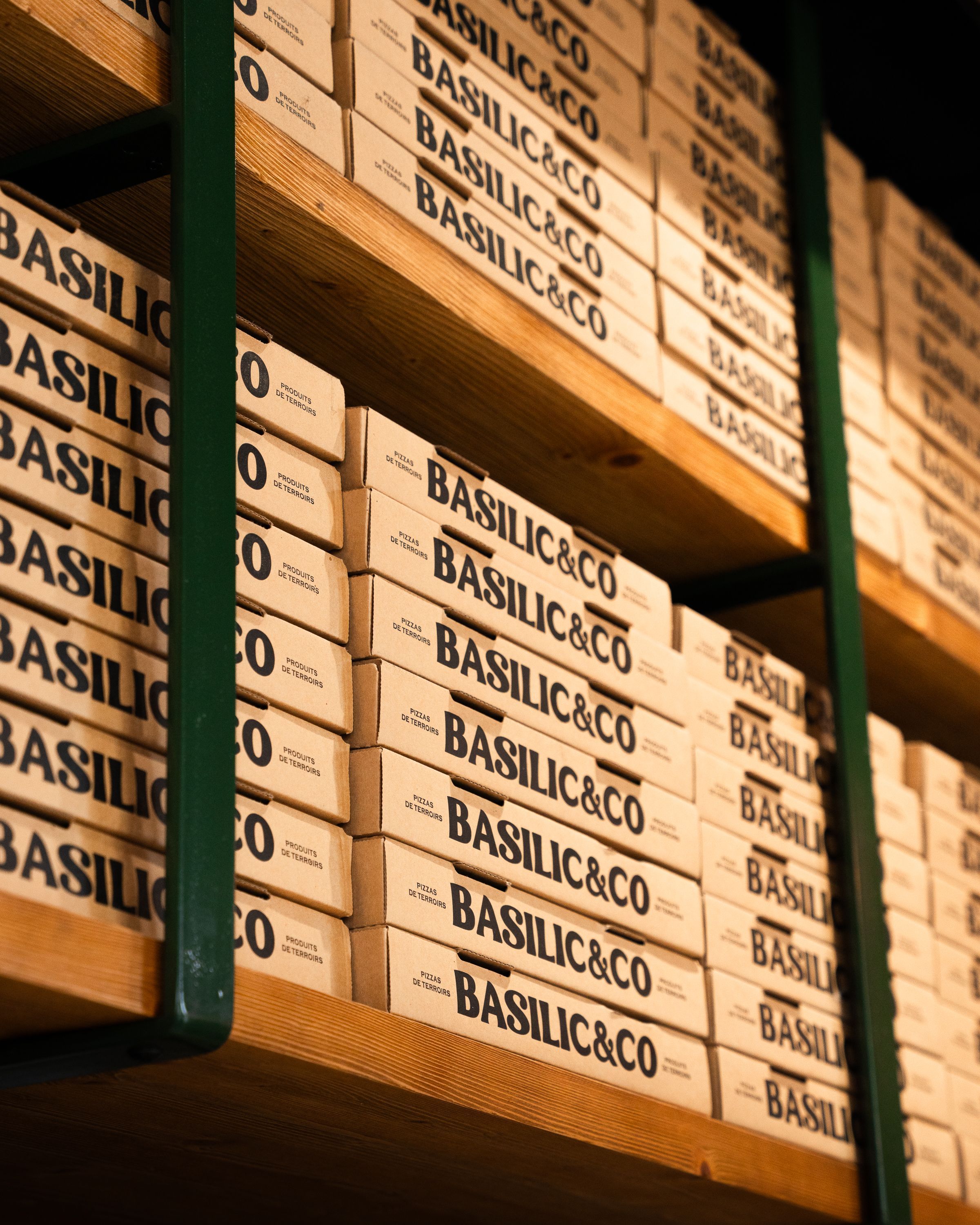 Étagère avec des boîtes à pizza de Basilic & Co, offrant des pizzas artisanales à emporter.