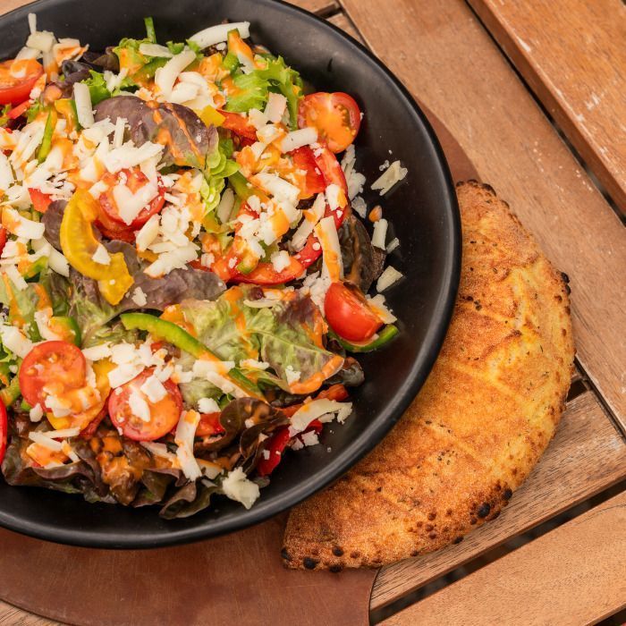 Salade fraîche variée avec fromage râpé, tomates cerises et légumes, accompagnée d'un calzone croustillant.
