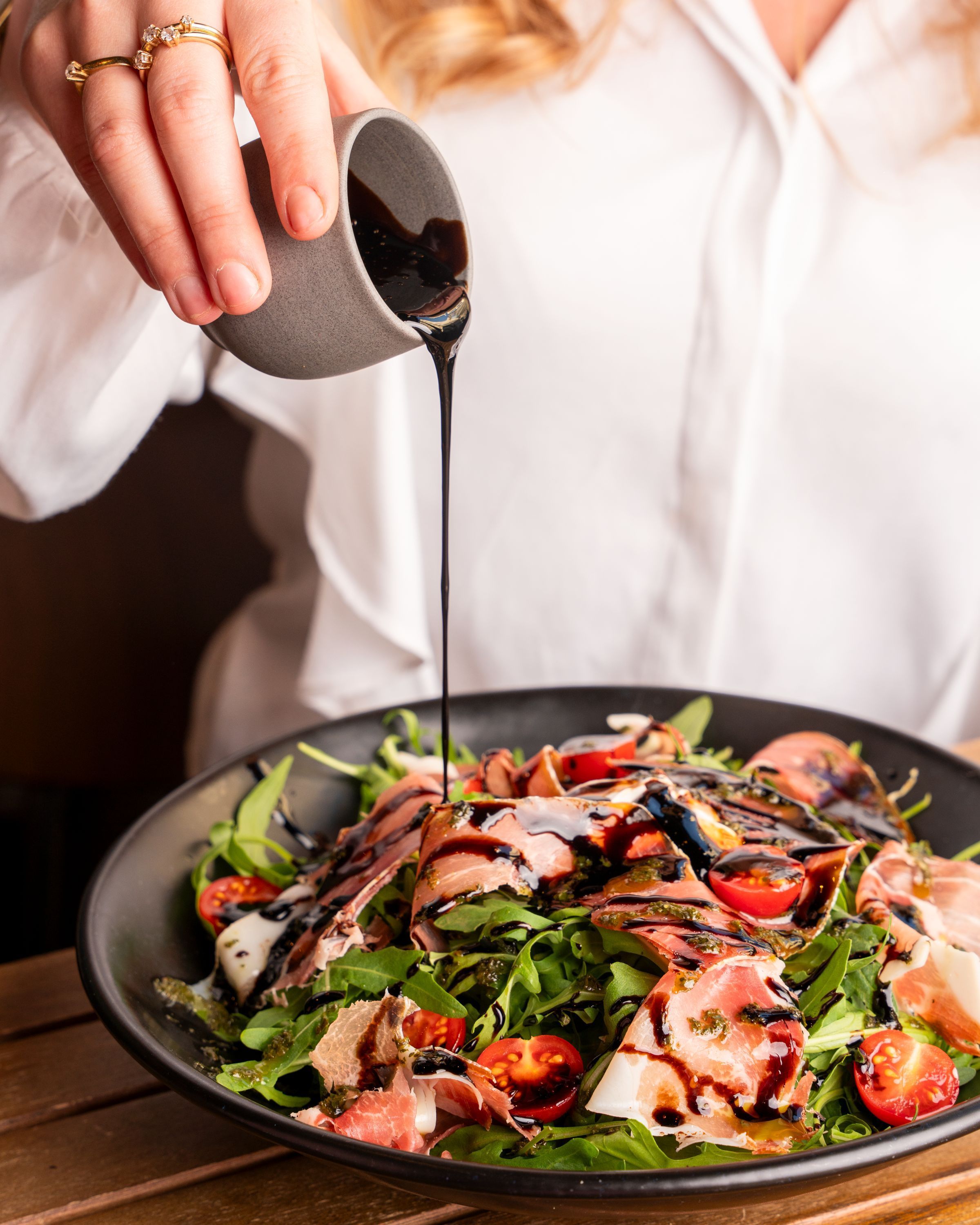 Salade fraîche avec roquette, tomates cerises, jambon cru et sauce balsamique versée à la main.