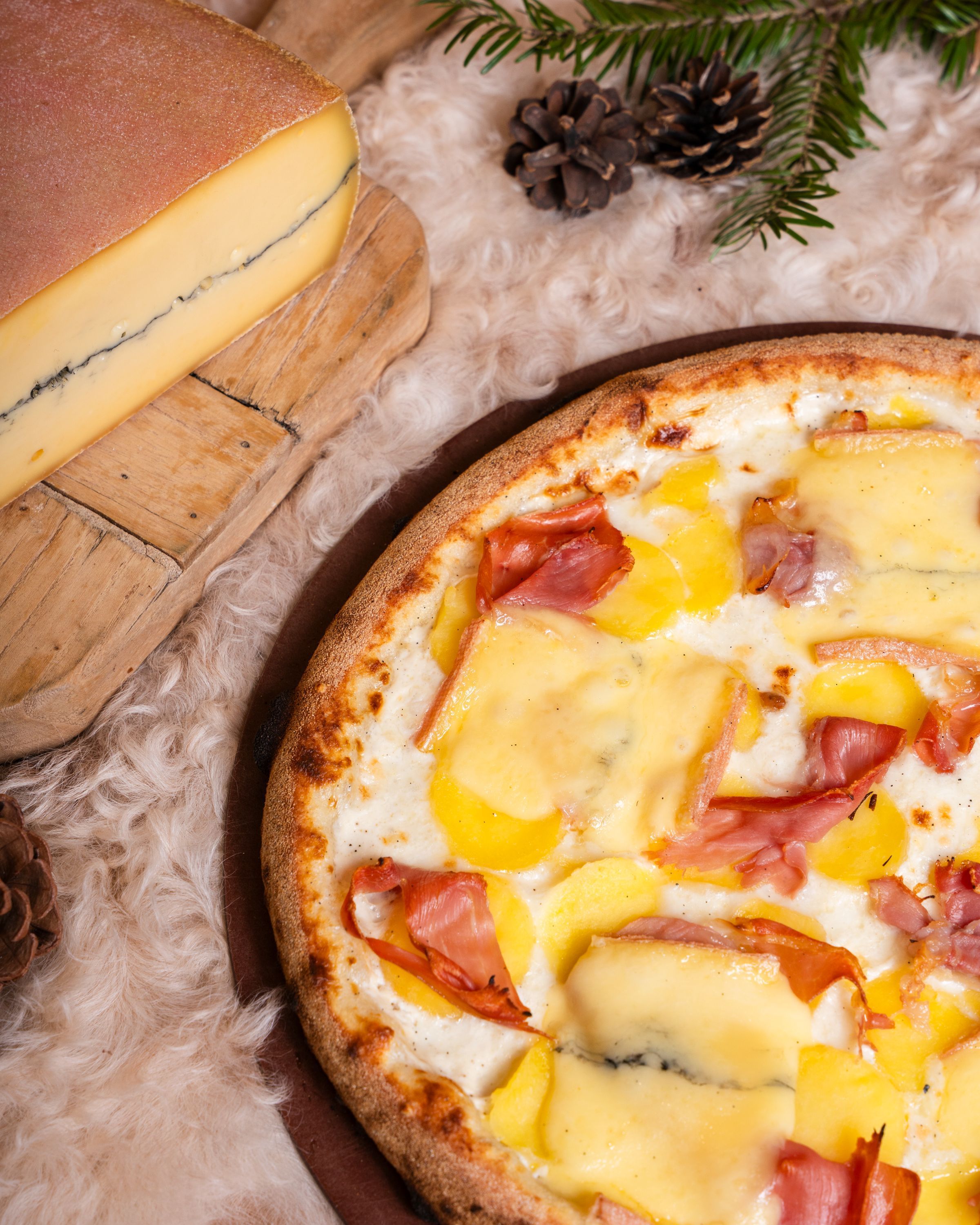 Pizza artisanale avec fromage, jambon et pommes de terre, servie avec des éléments de décoration rustiques.