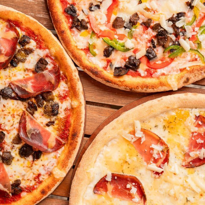 Pizzas artisanales avec différentes garnitures sur une surface en bois, à emporter ou en livraison.